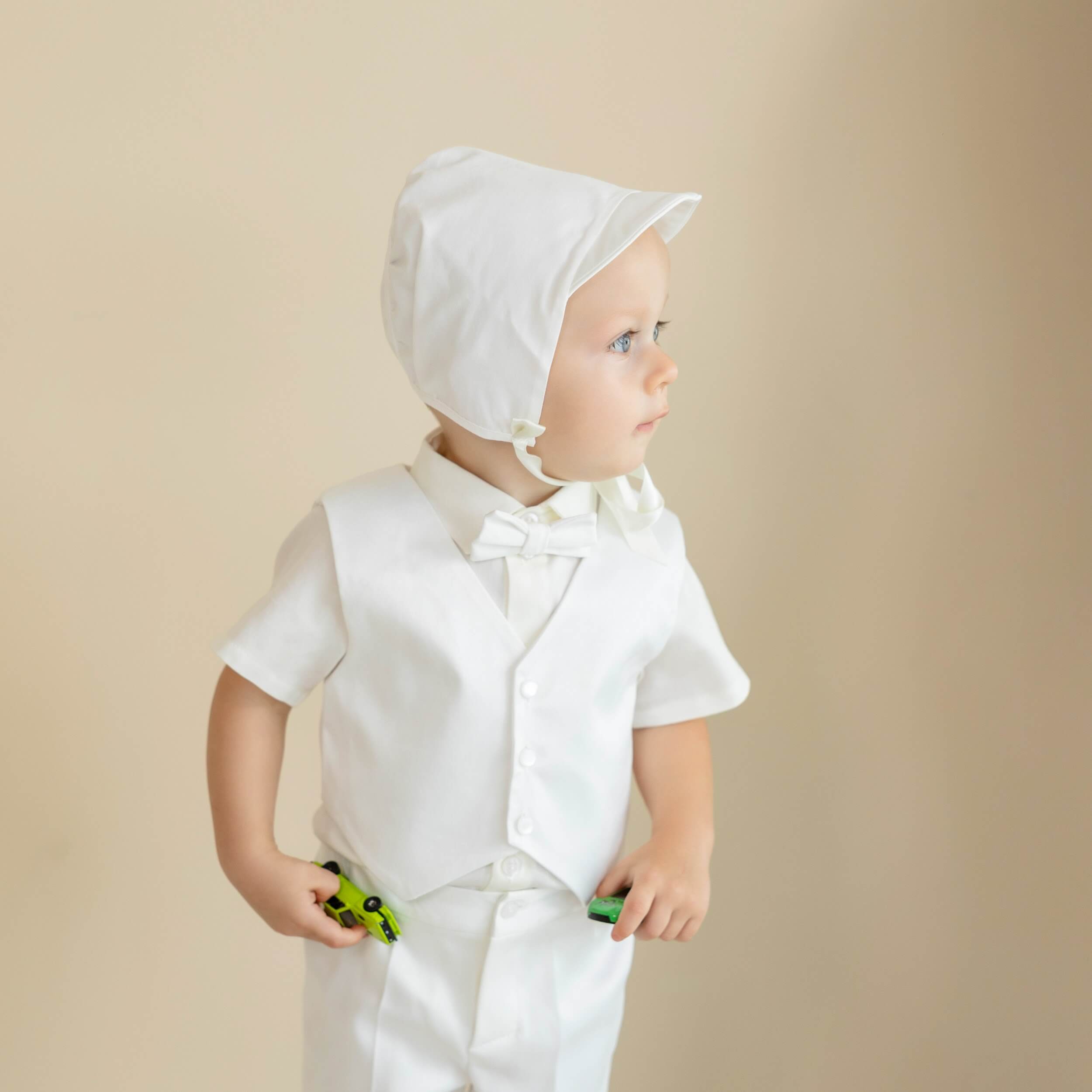 Child wearing a Baby Boy Christening Suit  with a bonnet on a beige background