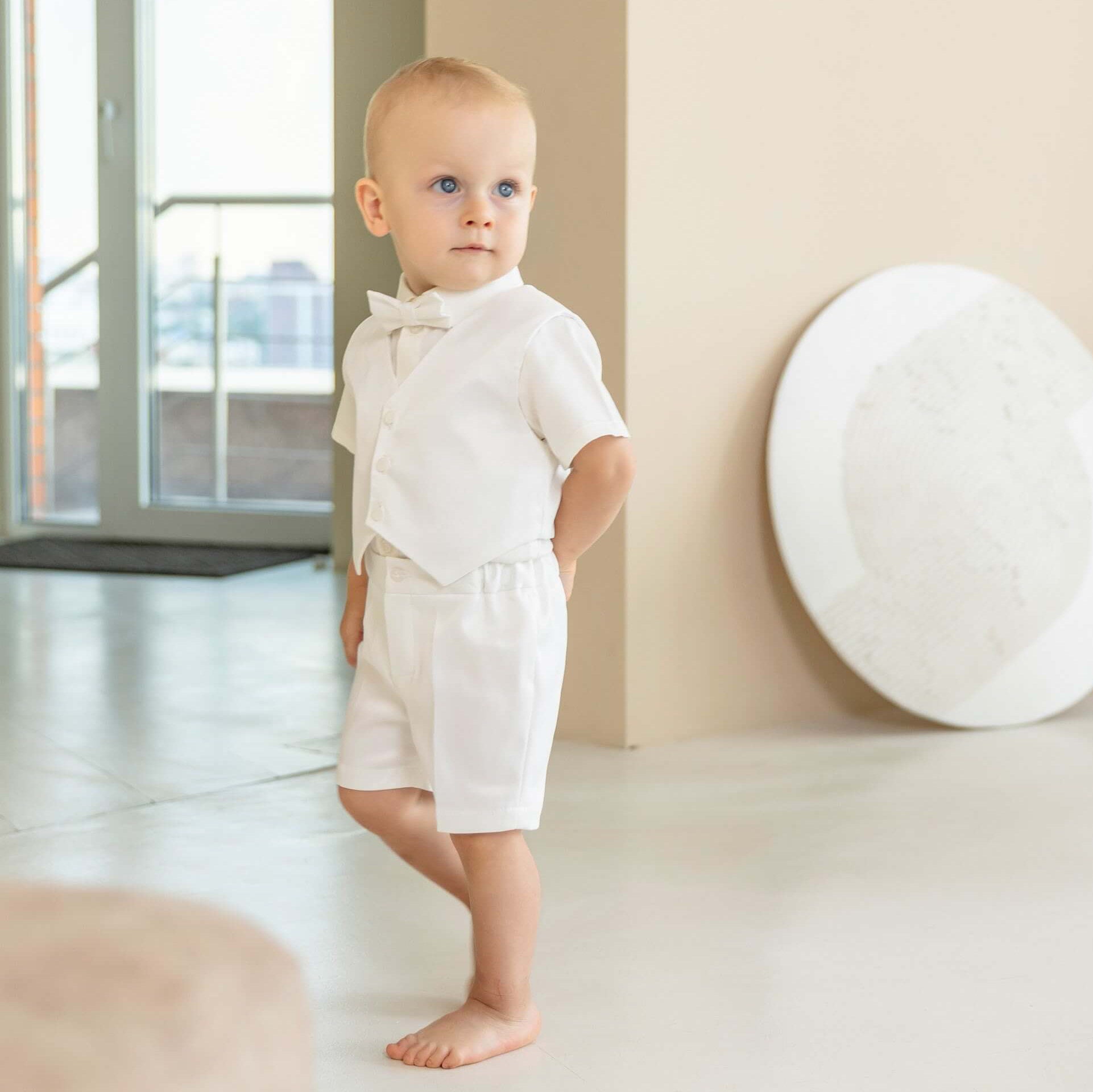 Baby in a Baby Boy Christening Suit standing in a minimalistic room with a large window.
