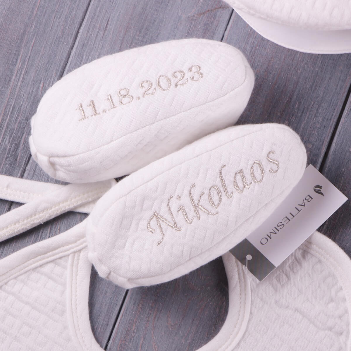 White baptism booties with name embroidered on them, placed on a wooden surface.