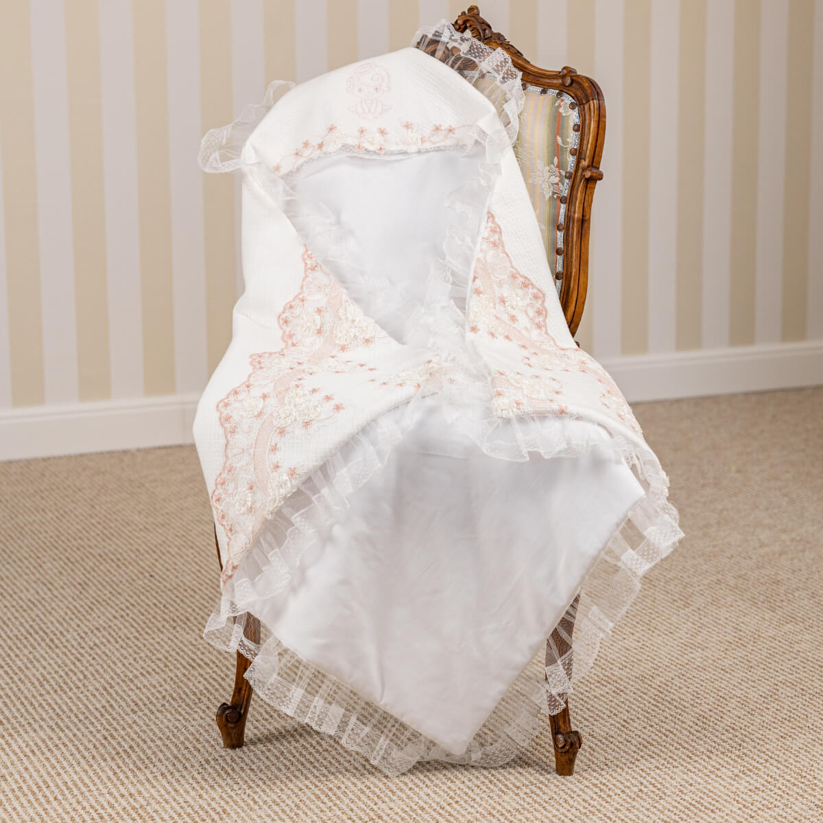 White lace baptism blanket on a wooden chair against a striped wall.