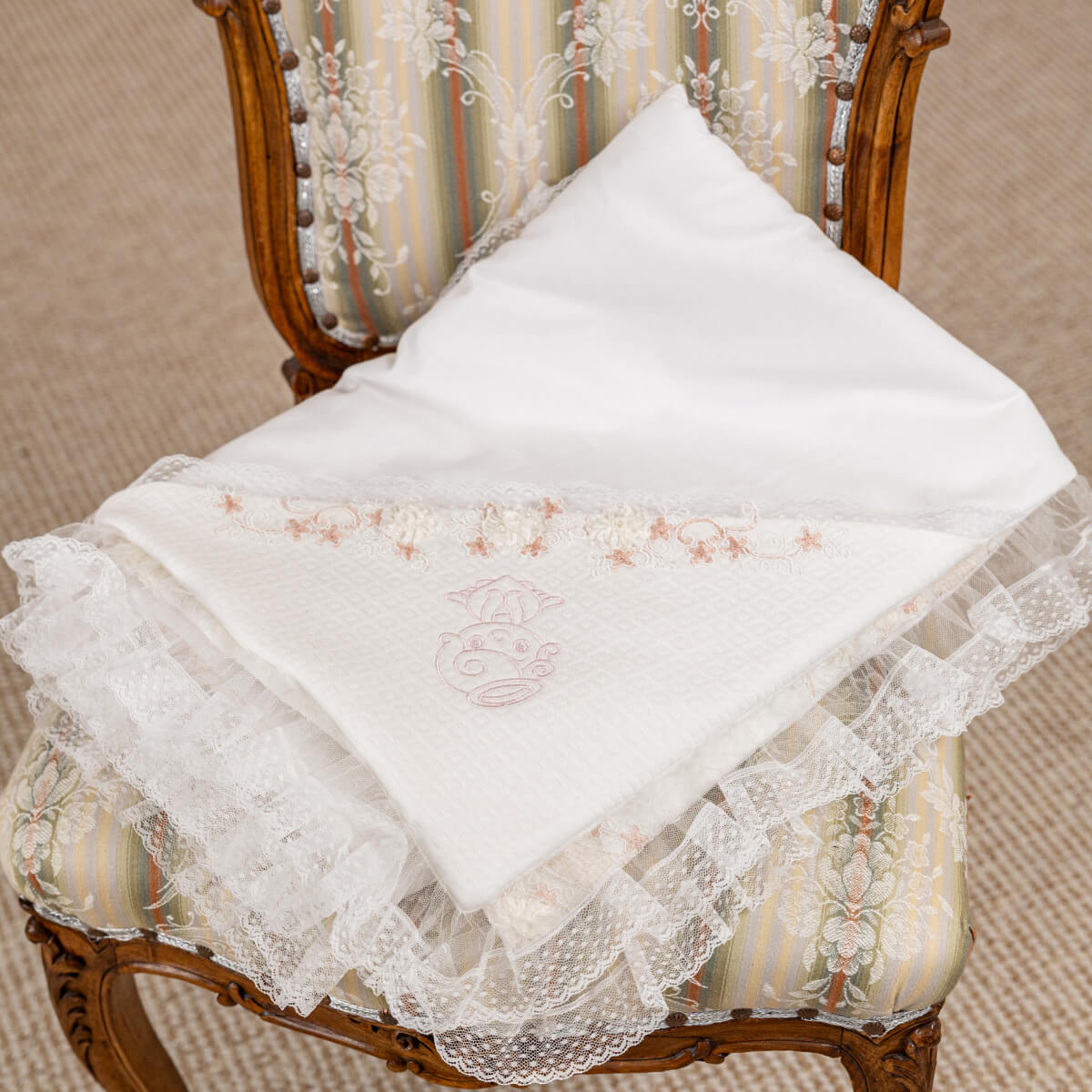 White lace-trimmed baptism blanket with embroidery on a decorative chair