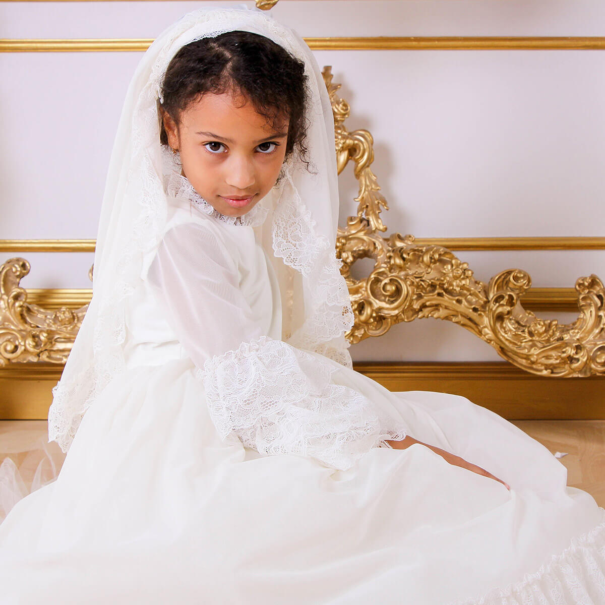 Young girl in Boho First Communion Dress with a gold ornate headboard in the background