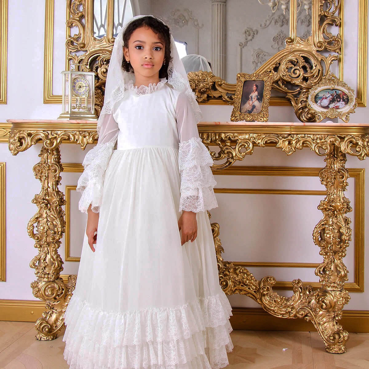 Young girl in Boho First Communion Dress standing in front of an ornate gold console table.